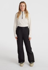 Zwarte sneeuwbroeken met een verstelbare tailleband, meerdere zakken en versterkte zoom. Gecombineerd met een crèmekleurige lange mouwen zip-up top.