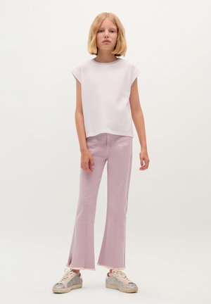 Hvid bomulds t-shirt med opslåede ærmer, parret med lyserøde slacks med flare og frynser i kanten, samt sølvfarvede sneakers.