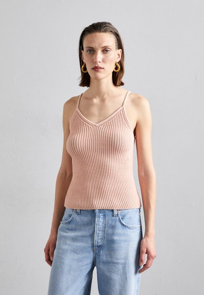 Helles rosa geripptes Tanktop mit V-Ausschnitt, dünnen Trägern und taillierter Silhouette. Kombiniert mit hellblauen, locker sitzenden Jeans.