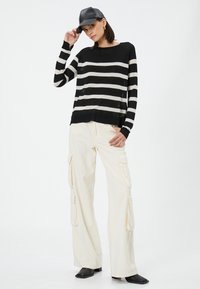 Stribet sweater i sort og hvid med en afslappet pasform, parret med crème farvede cargo bukser med sidelommer og sorte firkantede sko.