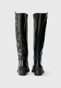 Schwarze Lederstiefel bis zum Knie mit glatter Oberfläche, ausgestattet mit einem seitlichen Reißverschluss und einem niedrigen Blockabsatz. Die Rückansicht hebt die Nähdetails hervor.