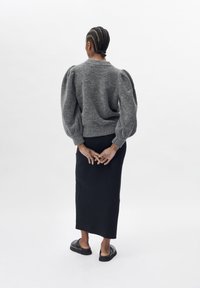 Szary sweter dziany z bufiastymi rękawami, zestawiony z długą czarną spódnicą i czarnymi butami wsuwanymi. Fryzura z warkoczami.