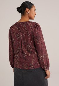 Blusa bordeaux con maniche a sbuffo, caratterizzata da un motivo giocoso di macchie scure e chiare. Tessuto morbido, scollatura rotonda e dettaglio di piega sul retro.