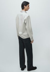 Camicia a maniche lunghe grigio chiaro con colletto, abbinata a jeans scuri a gamba dritta e scarpe nere. Texture liscia e design classico.