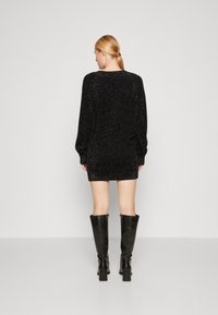 Mini abito nero scintillante con maniche lunghe e una vestibilità morbida. Indossato con stivali neri in pelle con tacco alti fino al ginocchio. Semplice scollatura tonda.