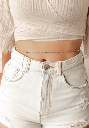 Zilveren kettingriem gedragen over witte beschadigde denim shorts, met een eenvoudig ontwerp van ovale schakels en een delicate textuur.