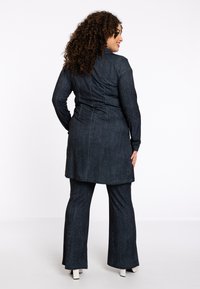 Donkerdenim tweeledig outfit met een lange tuniek en flared broek met een soepele textuur, achternaad details en witte hoge hakken.