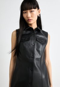 Vestito nero senza maniche realizzato in pelle, con abbottonatura frontale, due tasche sul petto e una silhouette sartoriale. Texture liscia.