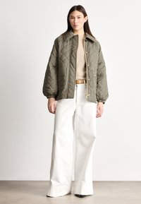 Sako s vzorem pepito s límečkem, elastickými manžetami a zipovým zapínáním, doplněné béžovým svetrem a bílými širokými kalhotami.