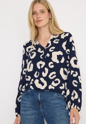 Blouse bleu marine avec imprimé léopard crème, décolleté en V, manches ballon longues et accents de boutons. Fabriquée en tissu léger.