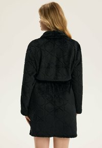 Czarny pikowany szlafrok z miękkiego materiału, z długimi rękawami, kołnierzykiem oraz paskiem w talii. Tekstura jest pluszowa, z wyraźnym wzorem w romby.