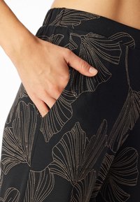 Pantaloni neri con un motivo floreale in cucitura beige; presentano una tasca laterale e una cintura elastica per il massimo comfort.