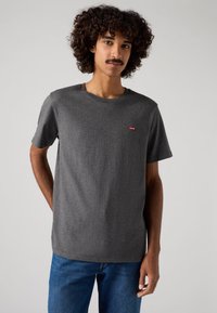 Grå kortærmet t-shirt lavet af blødt stof, med rund hals og et lille rødt logo på venstre bryst. Kombineret med blå denim jeans.