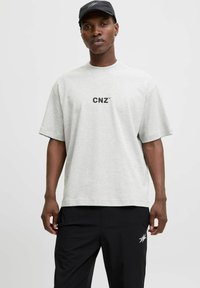 Lys grå bomulds t-shirt med korte ærmer, prydet med et sort "CNZ" logo på brystet, båret med sorte bukser. Glat tekstur, afslappet pasform.