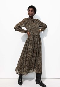 Robe longue à fleurs sombres avec une taille froncée, des manches bouffantes et un décolleté en trou de serrure. Portée avec des bottines noires.