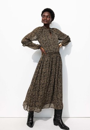 Robe longue à fleurs sombres avec une taille froncée, des manches bouffantes et un décolleté en trou de serrure. Portée avec des bottines noires.