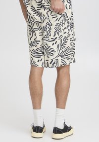 Cream shorts with a black leaf pattern, featuring a relaxed fit and side pockets. Casual footwear with white socks completes the look.
