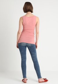 Rosa ärmlös topp tillsammans med blå skinneyjeans. Toppen har en figursydd design och jeansen har en fransad nederkant med fickdetaljer.