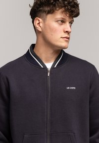 Granatowa bluza z suwakiem wykonana z mieszanki bawełny, z prążkowanym kołnierzem, białymi paskami oraz małym haftowanym logo "LEE COOPER".