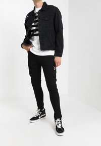 Chaqueta de mezclilla negra con detalle texturizado, camiseta gráfica blanca, pantalones ajustados negros con acento de cremallera y zapatillas altas negras.