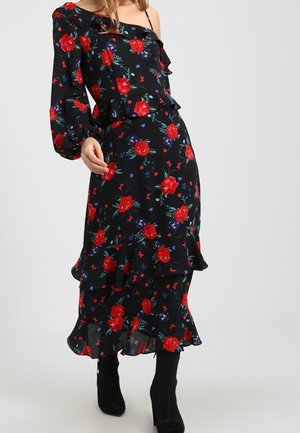 Vrouw die een zwarte bloemige jurk draagt met rode rozen, lange pofmouwen, geplooide zoom, gecombineerd met zwarte laarzen met hak.