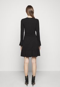 Abito lungo nero a maniche lunghe con orlo arricciato, vita arricciata e zip sul retro. Realizzato in tessuto leggero, con una consistenza liscia.