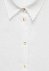 Biała lniana koszula z klasycznym kołnierzykiem, z sześcioma guzikami przypominającymi perły z przodu, wykonana z teksturowanej, lekkiej tkaniny.