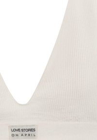 Krämfärgad ribbad bralette med en djup V-ringning och en etikett som läser "LOVE STORIES OH APRIL" nära botten.