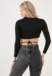 Black cropped long-sleeve top with an open back, paired with high-waisted grey denim jeans featuring a classic five-pocket design.