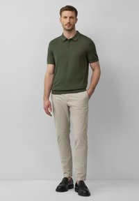 Oliwkowa koszulka polo z krótkim rękawem, w zestawieniu z jasnobeżowymi spodniami i czarnymi mokasynami. Prosty design, dopasowany krój, minimalne detale.