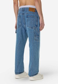 Vil�ágoskék farmer cargo nadrág, laza fit-vel, több zsebbel, texturált anyaggal és egy barna címkével a hátsó derékrészen.