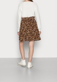 Ruskea leopardi-kuosiska skirt, jossa on joustava vyötärö, yhdistettynä valkoisiin nilkkureihin, joissa on kuvioitu pohja, ja kevyeseen valkoiseen villapaitaan.