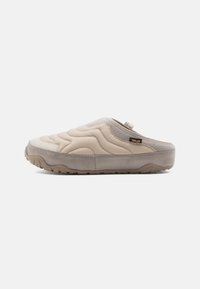 Beige slip-on klip med quiltet overdel, teksturerede ruskind detaljer og en gummisål med skridsikre mønstre, designet til komfort og nemhed.