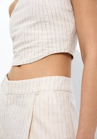 Top senza maniche beige a righe e pantaloni a vita alta coordinati su una persona, che mostra una vista laterale del ventre e del braccio.