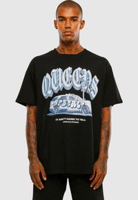 Black graphic t-shirt featuring blue lettering that reads "QUEENS" and an illustrated van with graffiti. Short sleeves and relaxed fit.
