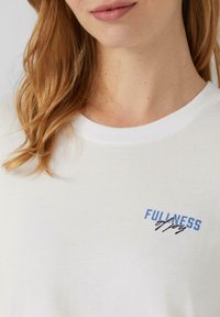 Witte katoenen T-shirt met een ronde hals, korte mouwen en een blauwe grafische tekst "FULLNESS of Joy" op de borst.