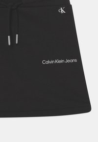 Mustapohjainen puuvillahame, jossa on nyöri vyötäröllä, hopeaosia ja valkoisella brodeerattu "Calvin Klein Jeans" -logo alareunassa.