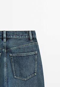 Jean en denim bleu foncé à taille haute, avec deux poches arrière et des coutures renforcées le long des coutures. Texture douce avec une légère décoloration.