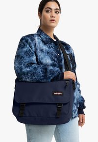 Marine Messenger Bag mit zwei schwarzen Riemen und einem Klappdeckel. Hergestellt aus strapazierfähigem Stoff, verfügt sie über ein Logopatch und eine glatte Textur.