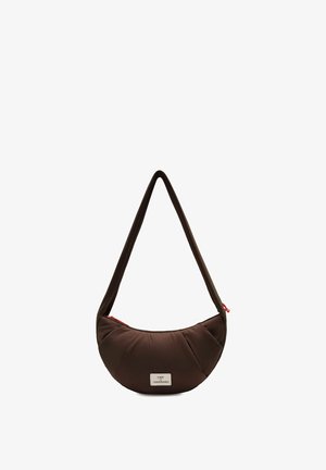 Bruine schoudertas in de vorm van een halve maan met een lange riem en een klein wit label aan de voorkant, tegen een witte achtergrond.