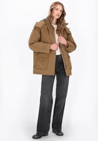 Bruine geïsoleerde parka met een ritssluiting en knopen, grote zakken, afneembare capuchon en grijze voering. Gecombineerd met zwarte wijde jeans en laarzen.