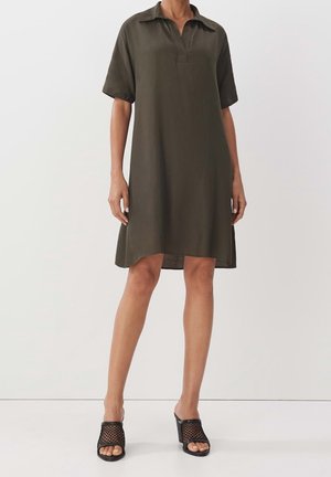 Olivinvihreä, lyhythihainen paitamekko, jossa on kaulus ja suora malli. Yhdistetty teksturoituihin mustiin korollisiin sandaaleihin. Yksinkertainen, minimalistinen muotoilu.