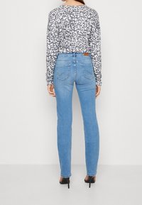 Top de leopardo gris y negro de manga larga combinado con jeans ajustados de un azul claro, que cuentan con bolsillos traseros y detalles de costura sutiles.