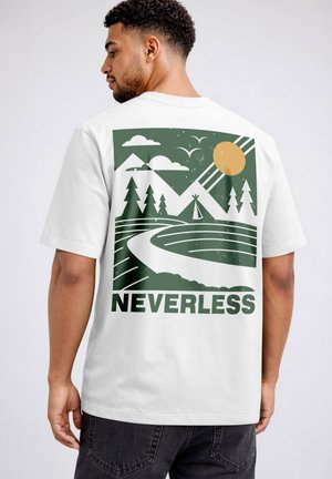 Man wearing white t-shirt with green and yellow nature graphic featuring mountains, trees, sun, birds, path, and the word "NEVERLESS" on back.