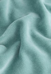 Tessuto teal morbido e texturizzato con una leggera lucentezza, che mostra delicate pieghe e onde, suggerendo flessibilità e calore.