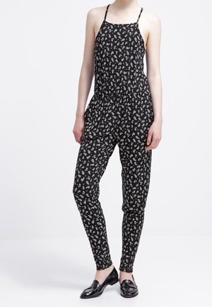 Combinaison noire avec un motif paisley, dotée de fines bretelles, d'une taille élastique et de jambes fuselées. Le matériau semble léger et texturé.