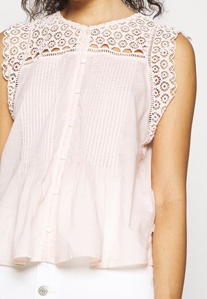 Blusa rosa chiaro con yoke in pizzo decorativo, chiusura frontale con bottoni e texture plissettata. Presenta un design senza maniche e un tessuto morbido e fluido.