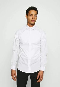 Camisa branca de botão, feita de um tecido suave, com colarinho pontudo, mangas longas e um design minimalista. Sem padrões ou acentos visíveis.