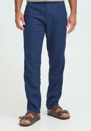 Marineblå linnedbukser med en lige ben-snit og forlommer, kombineret med brune åbne tå-sandaler med en rem og spænde.