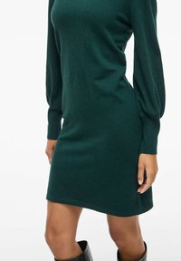 Vestido de punto verde con mangas largas y abullonadas, y un corte relajado. Textura suave, hasta la rodilla, puños acanalados y escote redondo.